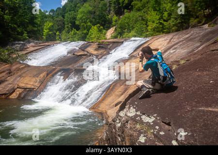 Escursionista con zaino che scatta foto di una cascata in una posizione panoramica Foto Stock