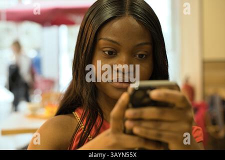Giovane donna nera che naviga nei negozi online sul suo smartphone mentre fa shopping in un centro commerciale, godendo della comodità della comunicazione digitale e esplorando la Foto Stock