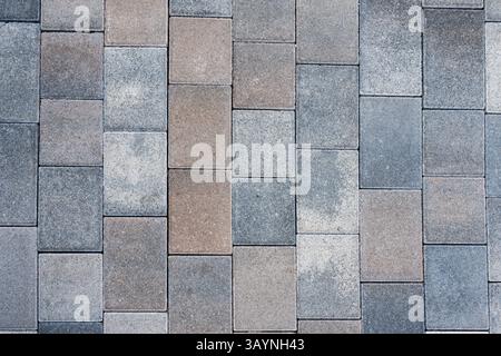 Vista ravvicinata di un muro o di un marciapiede in pietra rettangolare o mattoni in varie tonalità di grigio, rosso e marrone. La consistenza ruvida e ripetere Foto Stock