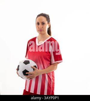 Giovane donna adulta che tiene il pallone da calcio in uno studio al coperto e indossa una maglia a righe rosse e bianche Foto Stock
