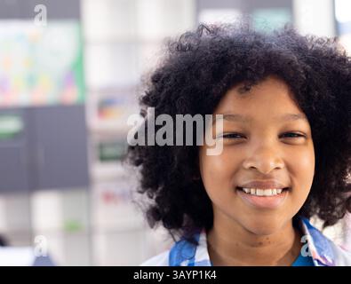 Ragazzo afroamericano sorridente e che guarda la macchina fotografica nel corridoio della scuola, con armadietti colorati Foto Stock
