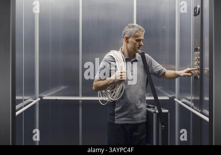 Elettricista professionista in piedi nell'ascensore e premendo un pulsante sul pannello di controllo Foto Stock