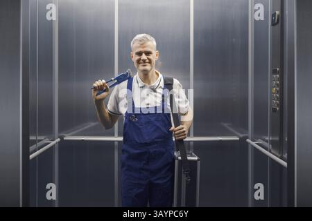 Ritratto di un idraulico professionista sorridente in piedi in un ascensore e tenendo in mano le attrezzature Foto Stock