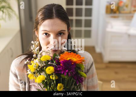 Donna che tiene in mano un vivace bouquet di fiori misti nel soggiorno, con margherite arancioni e mamme Foto Stock