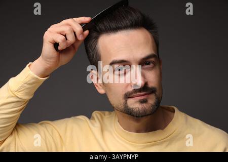 Bell'uomo che si pettina i capelli su sfondo scuro Foto Stock