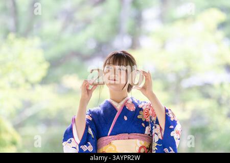 Una città locale in Giappone in un giorno d'estate piovoso. Una donna giapponese che indossa un kimono adolescente blu in un giardino tradizionale. Ha blocchi di 2 e 0 in lui Foto Stock