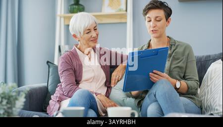Parlando, donna anziana e figlia con documento, salotto o lettura per benefici di assicurazione sanitaria. Casa, madre anziana e documenti con informazioni Foto Stock
