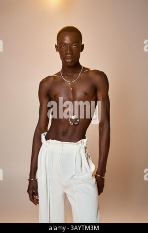 Un giovane uomo sicuro di sé con un abbigliamento elegante si pone su uno sfondo minimalista, trasudando fascino ed eleganza. Foto Stock