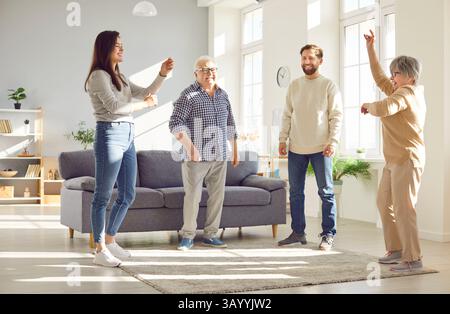 Genitori anziani felici che si divertono con i loro figli adulti che ballano nel soggiorno di casa Foto Stock