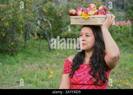 Una donna che porta con grazia le mele nel suo vivace e colorato abbigliamento tradizionale Foto Stock