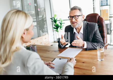 Uomo d'affari anziano e collega donna in un ufficio che ha una discussione professionale durante la revisione dei documenti Foto Stock