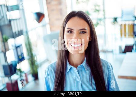 Donna sicura di sé e professionale che sorride in un moderno ambiente d'ufficio con luce naturale, per un comportamento positivo e accessibile. Foto Stock