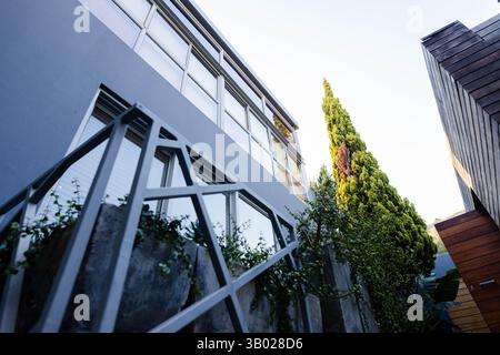 La moderna facciata dell'edificio presenta finestre blu-grigie nel cortile, con ringhiere geometriche e fioriere Foto Stock