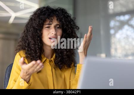 Una donna frustrata con capelli ricci si muove con forza durante una videochiamata, sembrando turbata e confusa. Foto Stock