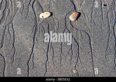 Ciottoli e motivi nella sabbia, in una spiaggia lungo la costa del Pembrokeshire Foto Stock