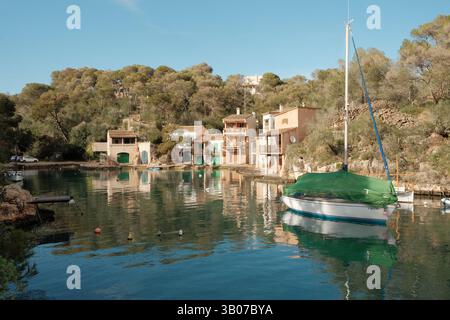 Una barca a vela verde e bianca che galleggia nel tranquillo porto di Cala Figuera, Maiorca. Circondato dalla foresta mediterranea e dai tradizionali pescatori Foto Stock