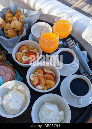 Colazione continentale con caffè, succo d'arancia, frutta fresca, yogurt, carne e formaggio e pasticcini su un vassoio all'aperto sul balcone dell'hotel. Foto Stock