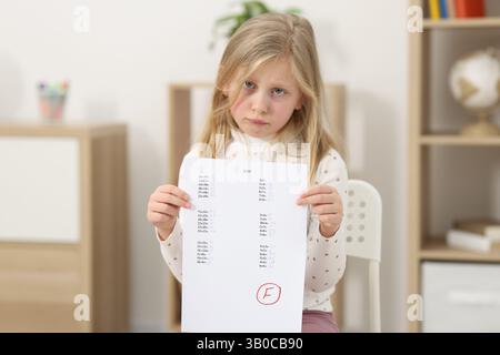 Grado scolastico. Ragazza triste che tiene in mano il foglio delle risposte con la lettera F in casa Foto Stock