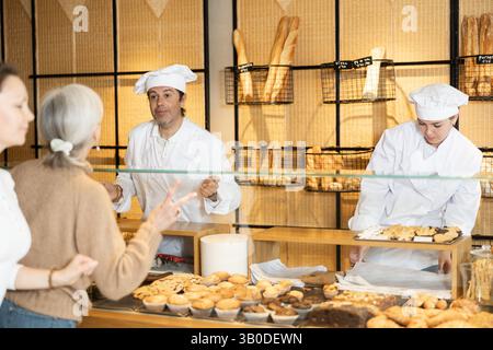 Gentile proprietario di una panetteria che serve i clienti dietro una vetrina di vetro Foto Stock