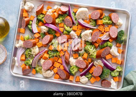 Piatto di verdure e salsicce pronto per essere cotto al forno con cavolfiore, broccoli e cipolla rossa Foto Stock