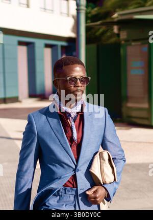 Un Dapper Man vestito con un elegante outfit con occhiali da sole e un accessorio sciarpa Foto Stock