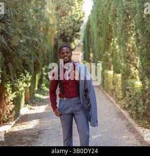 Un uomo elegante vestito con un abbigliamento elegante che cammina in modo informale attraverso un bellissimo sentiero lussureggiante Foto Stock