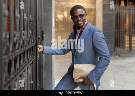 Un uomo elegante posa con sicurezza in un ambiente urbano indossando occhiali da sole e abbigliamento casual Foto Stock