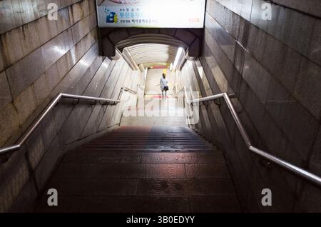 Busan, Corea del Sud - 19 marzo 2018: Una scalinata ben illuminata scende in un moderno tunnel pedonale sotterraneo, costruito con pareti pulite in cemento ed eq Foto Stock