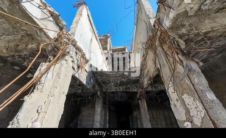 Una vista ad angolo basso di un edificio abbandonato e fatiscente con armature esposte e cemento sbriciolato contro un cielo azzurro. Foto Stock