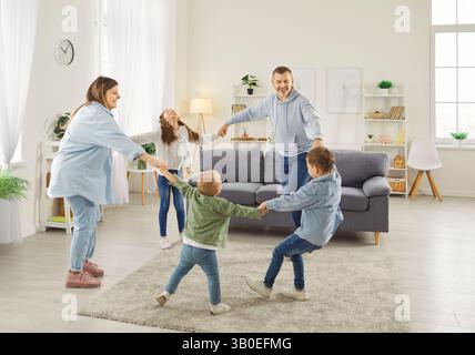 Famiglia felice che si tiene per mano e balla in tondo nel soggiorno, divertendosi insieme. Foto Stock