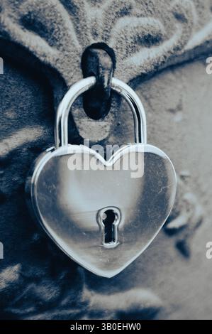 primo piano, immagine verticale in bianco e nero di lucchetto di sicurezza a forma di cuore argento o cromato bloccato sulla porta in metallo con riflessi vintage Foto Stock