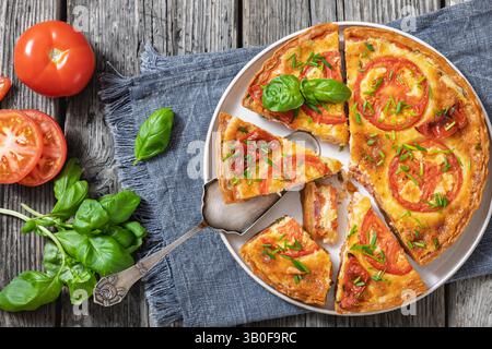 Torta di pomodoro italiano e pancetta su un tavolo in legno rustico con pala per torte, basilico fresco e pomodori, vista orizzontale, piatto, primo piano Foto Stock