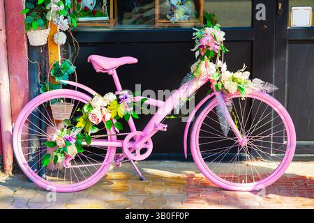 Vicino al negozio si trova una bicicletta urbana rosa decorata con fiori. Foto Stock