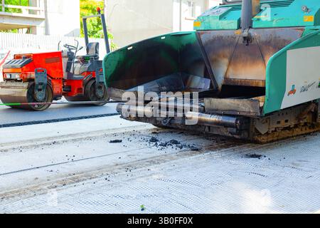 Un'asfaltatrice e un rullo stradale stanno lavorando per stendere nuovo asfalto sulla strada. Foto Stock