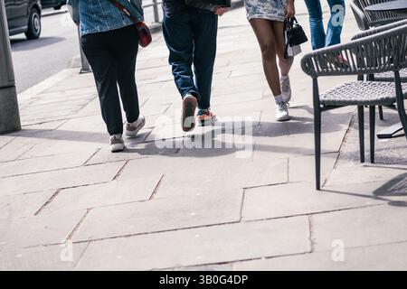 Pedoni anonimi che camminano sulla strada principale britannica - metà inferiore vista delle persone con spazio per la copia del testo Foto Stock