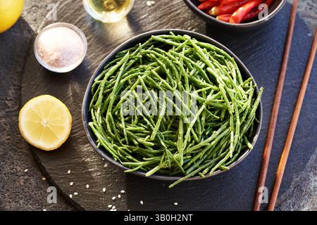 Alga verde Salicornia in un recipiente con sale, limone, semi di sesamo e peperoncino su fondo scuro» Foto Stock