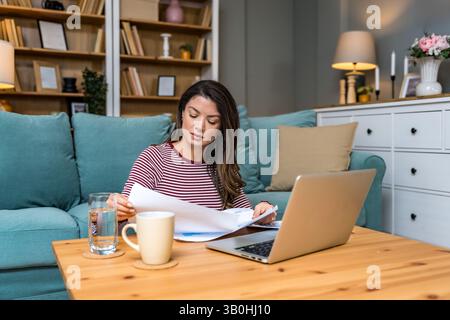 Crisi finanziaria. Giovane donna d'affari preoccupata, seduta a casa, che cerca di trovare una via d'uscita, calcolando le entrate e le spese della sua piccola dimensione globale Foto Stock
