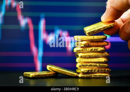 Primo piano con la mano che tiene una mano dorata fissa il grafico a candelabro. Contesto , concetto di fluttuazioni dei prezzi dell' oro. Foto Stock