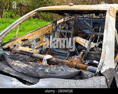 Vista laterale di una cabina completamente distrutta con sedili bruciati, telai metallici esposti, piantone dello sterzo arrugginito e interni ricoperti di cenere dopo un grave incidente Foto Stock