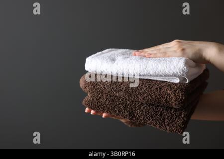 Donna con asciugamani puliti su sfondo grigio scuro, primo piano. Spazio per il testo Foto Stock