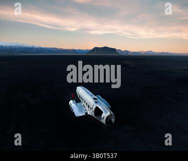 Il relitto abbandonato dell'aereo DC-3 della Marina americana sulla spiaggia di sabbia nera islandese di Solheimasandur, con una figura solitaria nel cielo rosso e pastello al tramonto. Foto Stock