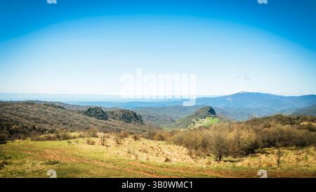 Tranquillo paesaggio primaverile a Kakheti, Georgia, caratterizzato da colline boscose, prati verdi lussureggianti e vette innevate lontane sotto un cielo azzurro Foto Stock