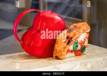 Milano, Italia - 12 aprile 2025: Borsa rossa a forma di cuore e pochette realistiche a fette di pizza nella boutique di Moschino. Accessorio di moda concettuale Foto Stock
