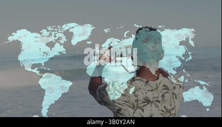 Mappa del mondo sulla vista posteriore dell'uomo africano ameriano che scatta foto dal suo smartphone in spiaggia Foto Stock