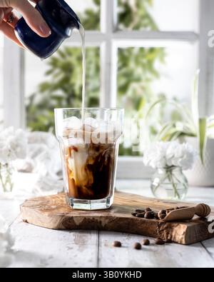 Caffè ghiacciato in un bicchiere con latte versato a mano Foto Stock