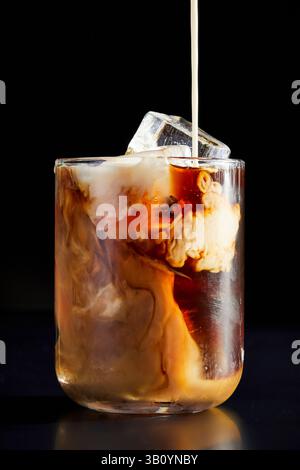 Caffè versato in un bicchiere su sfondo nero Foto Stock