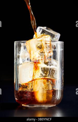 Caffè versato in un bicchiere su sfondo nero Foto Stock