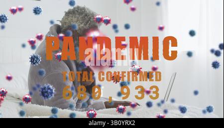 Uomo che lavora in felpa con cappuccio digitando su laptop argento in camera da letto, con grafica virus, spazio copia Foto Stock