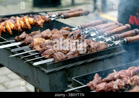 Succose spiedini di carne cucinati su spiedini di metallo con manici in legno. Pollo alla griglia e manzo su barbecue caldo con affumicatura. Preparazione del cibo di strada Foto Stock