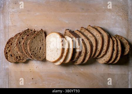 Assortimento di pane affettato fresco, compreso il grano intero bianco e la segale, disposti in fila su un tagliere in legno. Varietà di pane scuro e chiaro per san Foto Stock
